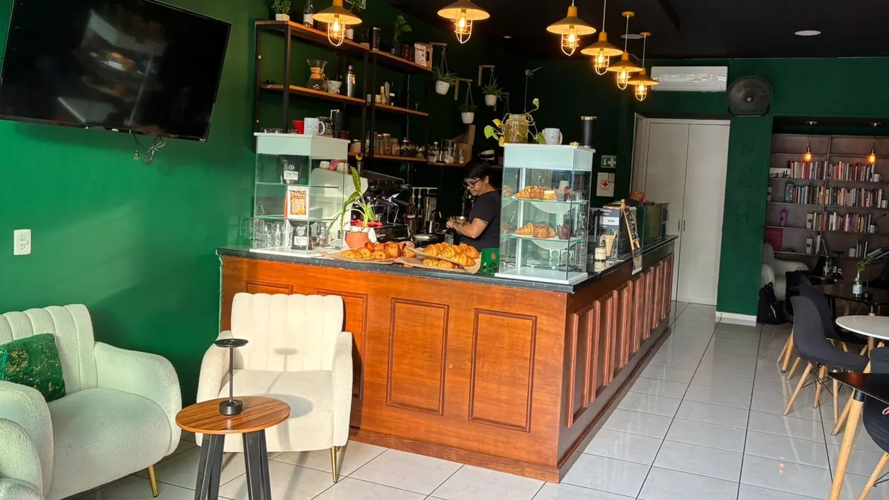 Interior de Cofradía: la barra de madera con la vitrina de panadería, las lámparas colgantes encendidas, las paredes verdes y el librero al fondo